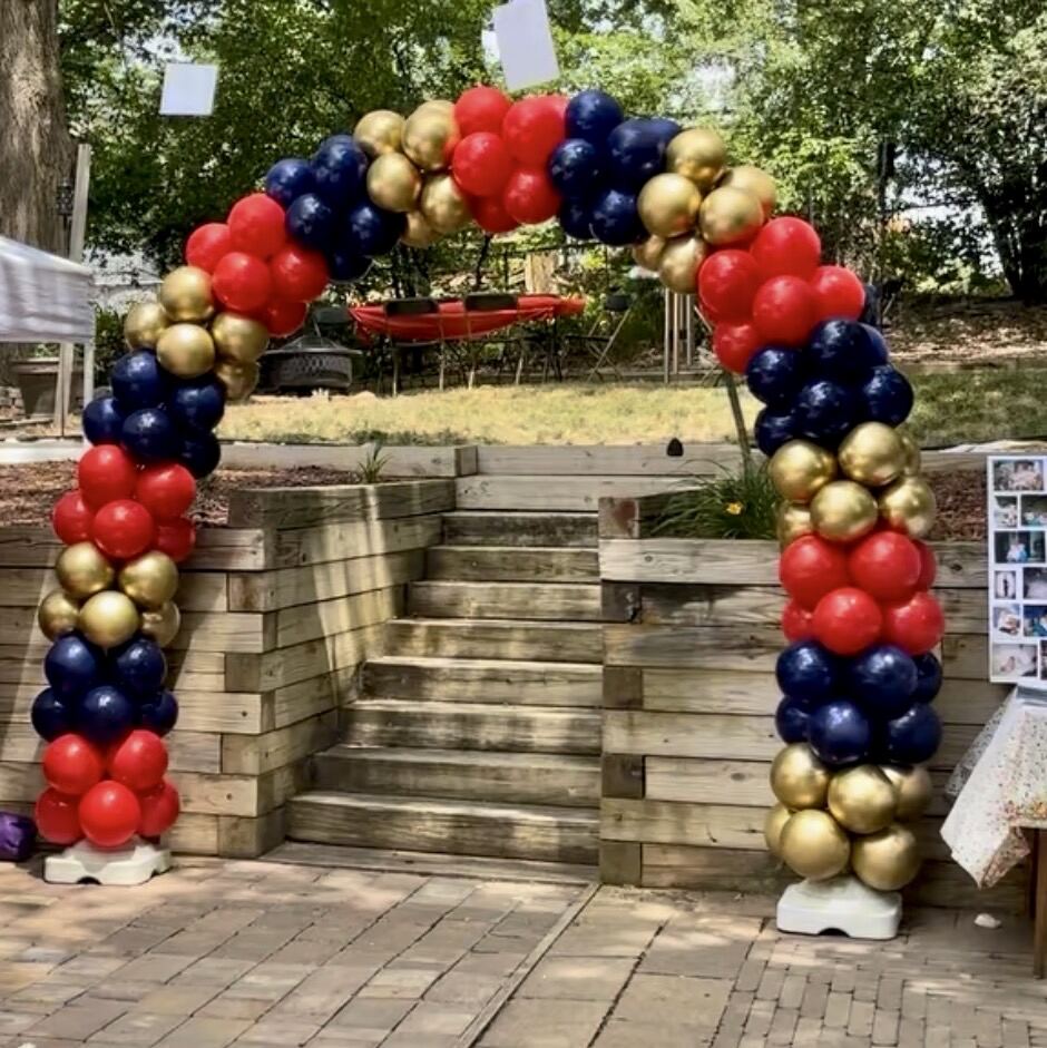 A classic red, navy, and gold balloon arch outdoors