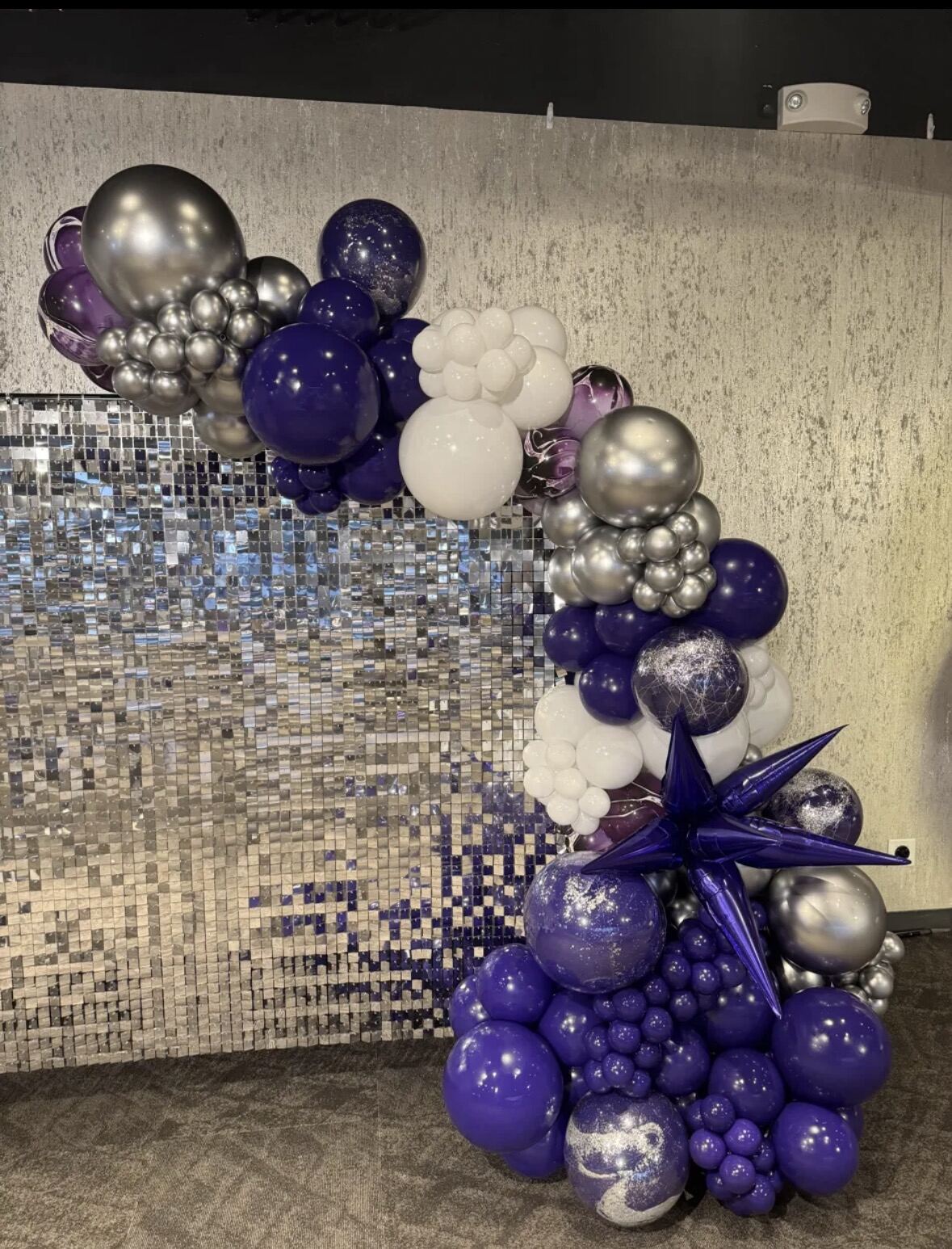 A purple, silver, and white balloon garland over a silver sequin backdrop