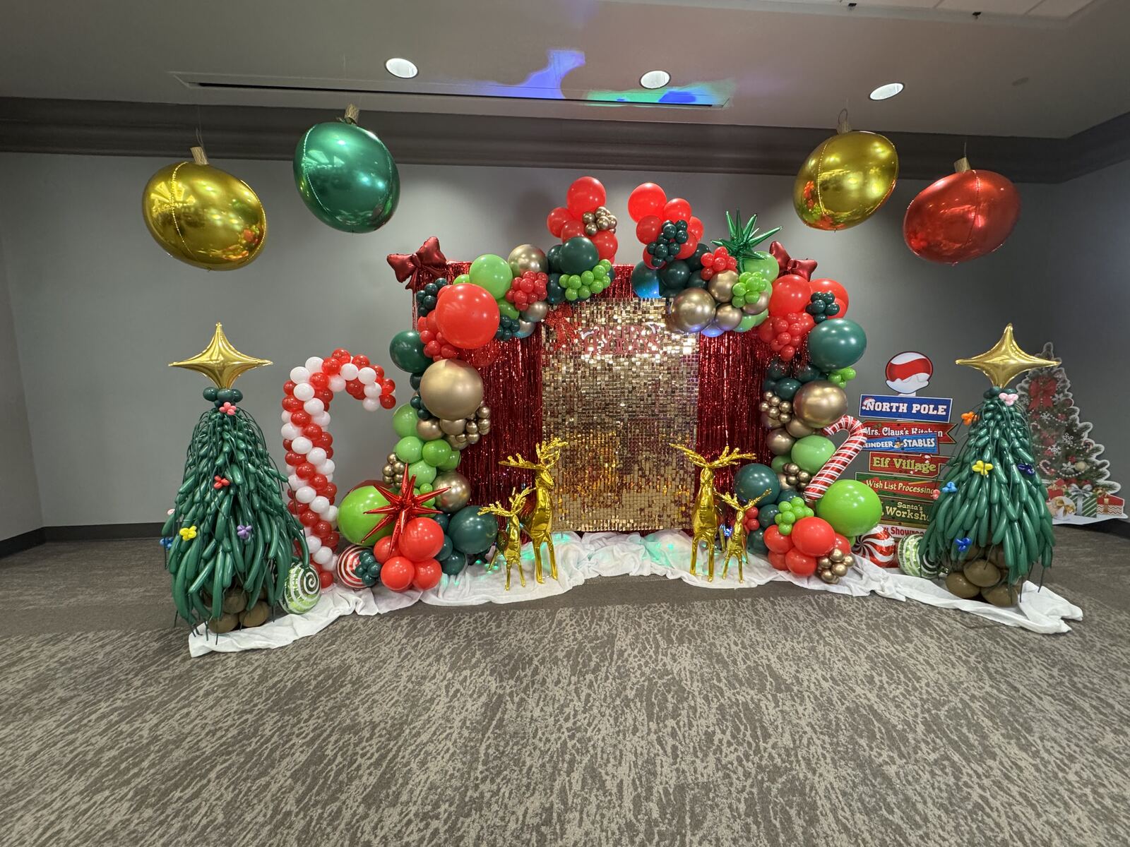 A red, green, and gold North Pole themed Christmas balloon backdrop with reindeer