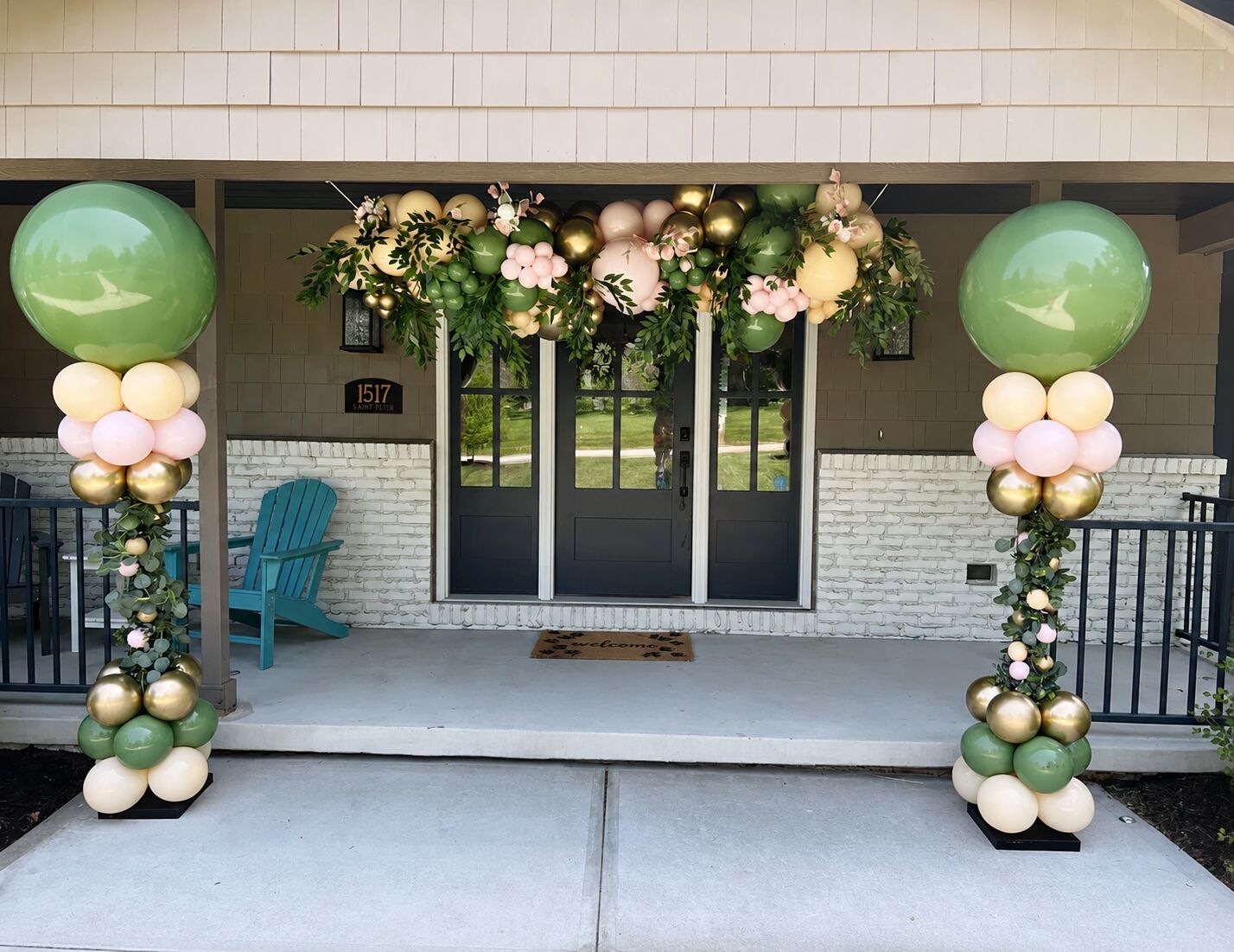 Green, gold, and blush balloon columns and a garland framing a front porch entrance